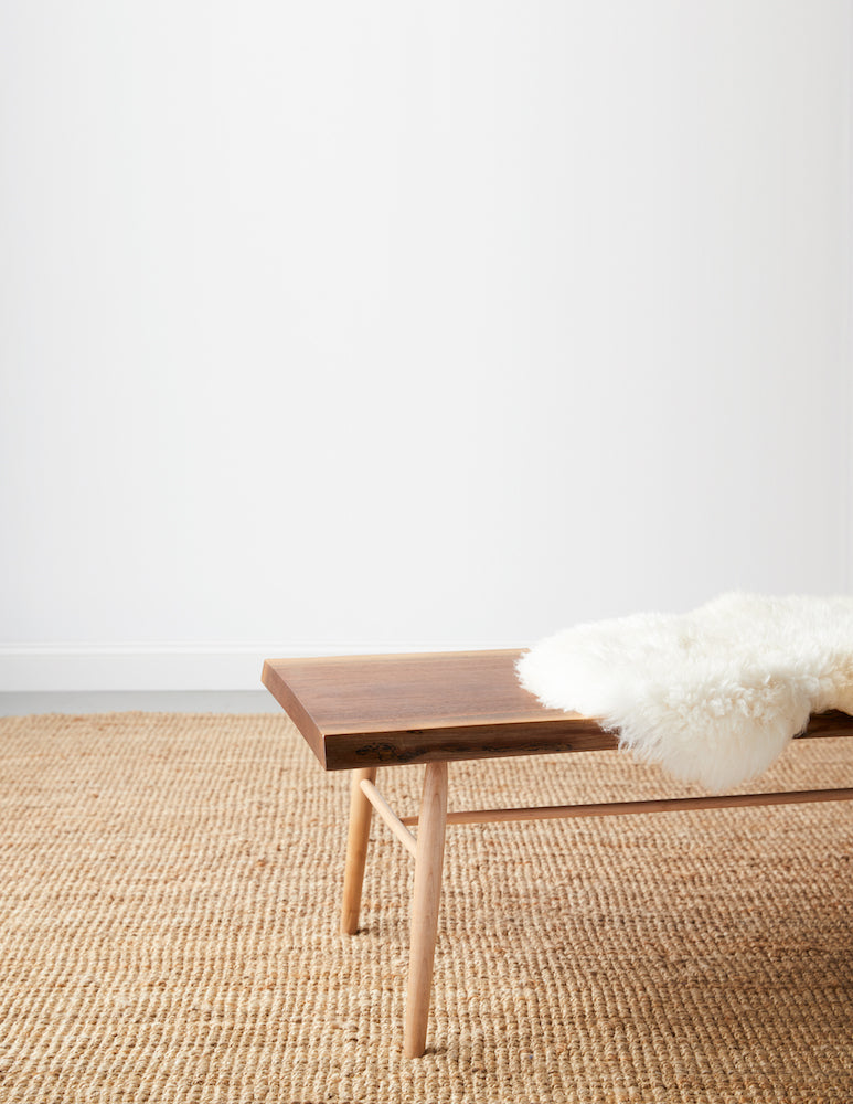Walnut live edge bench with maple round turned legs with white sheepskin cushion on beige woven rug