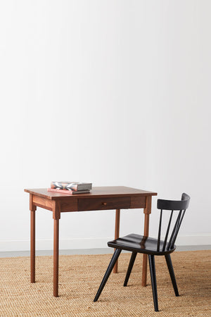 Small walnut MS1 desk with rounded legs, books on top, and one drawer paired with modern modern spindle chair