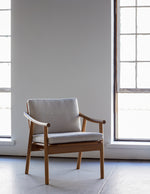 White oak lounge chair with rounded legs and curved arms with Knoll fabric cushions in front of large industrial windows