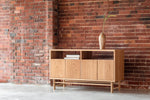 White oak Navarend Media Stand shown in white oak along brick wall