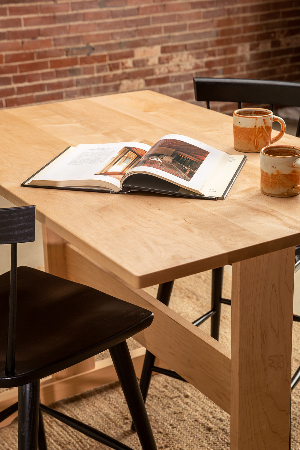 Coffee cups and an open book on the Acadia Breakfast Bar in maple with black counter stools