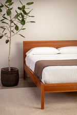 Minimalist bedroom with cherry Shiplap bed and shaker nightstand and a tree in the corner