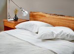 Bedroom furnished with Acadia nightstand, live edge bed in cherry made with white bedding and silver lamp