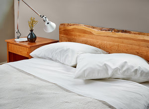 Bedroom furnished with Acadia nightstand, live edge bed in cherry made with white bedding and silver lamp