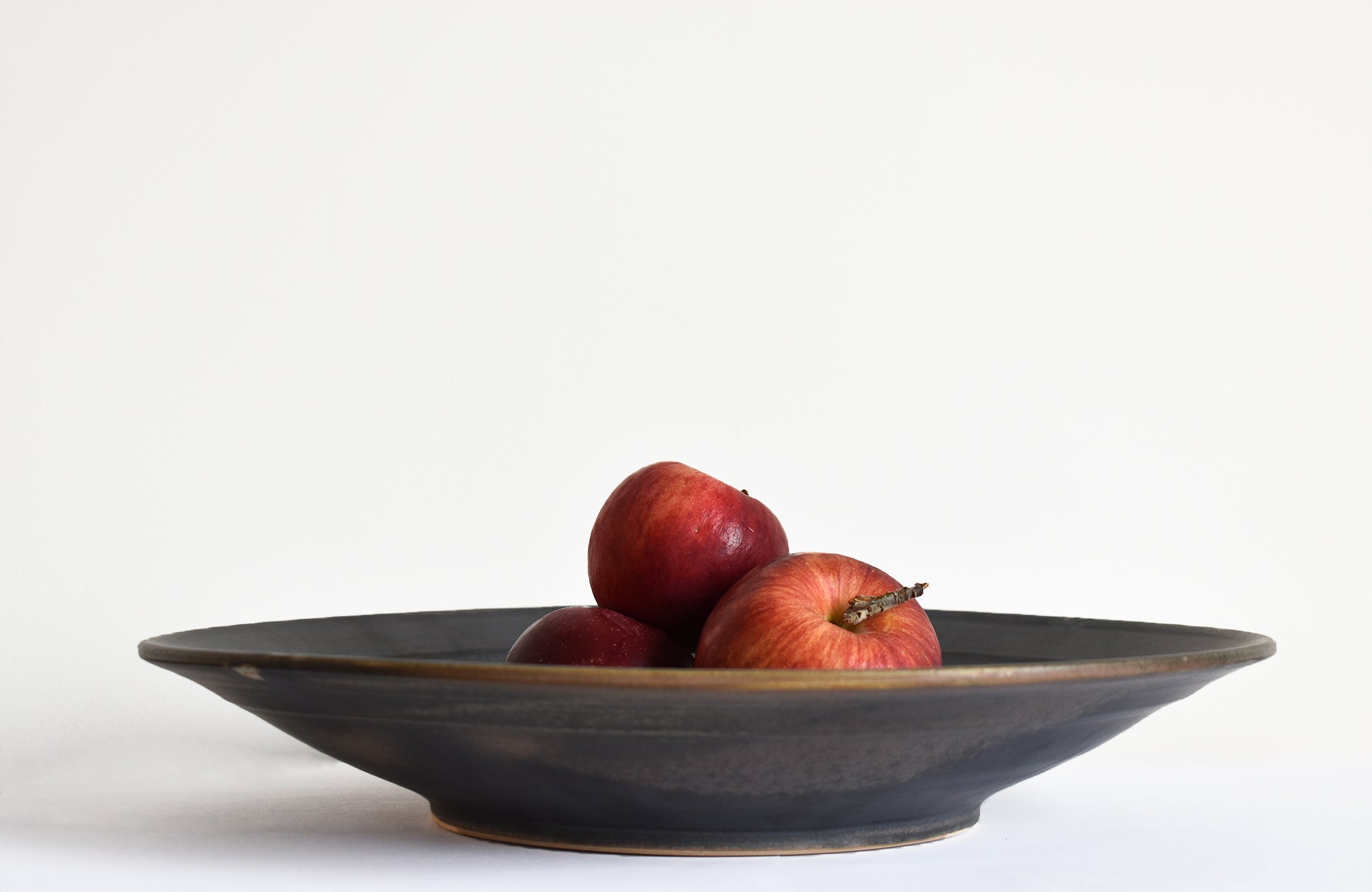 Hand thrown grey ceramic platter with three red apples in it
