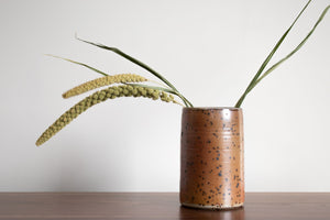 Speckled ceramic vase or utensil holder with grass coming out of top