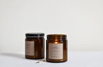 Two candles in amber glass jars, one with black lid and other with lit flame and burnt candle 