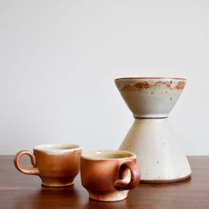 White hourglass shaped ceramic vase with two small brown espresso cups