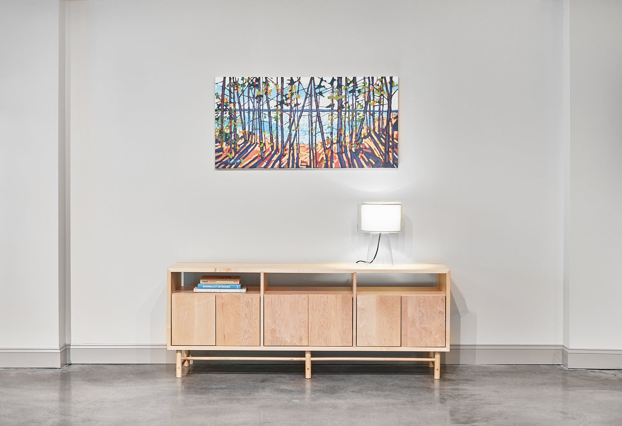 Industrial room with mid-century modern Navarend media case in solid maple with round legs and stretchers and an impressionism painting of trees