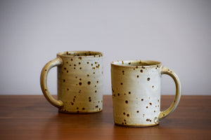 Two tall white ceramic mugs with dark spots