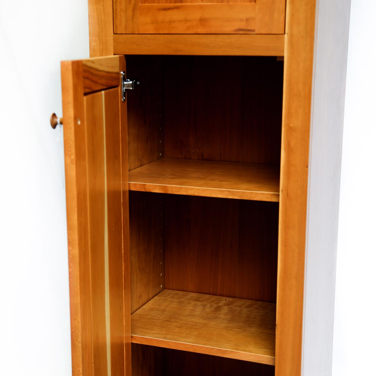Open door of cherry chimney cupboard showing storage space and two shelves inside